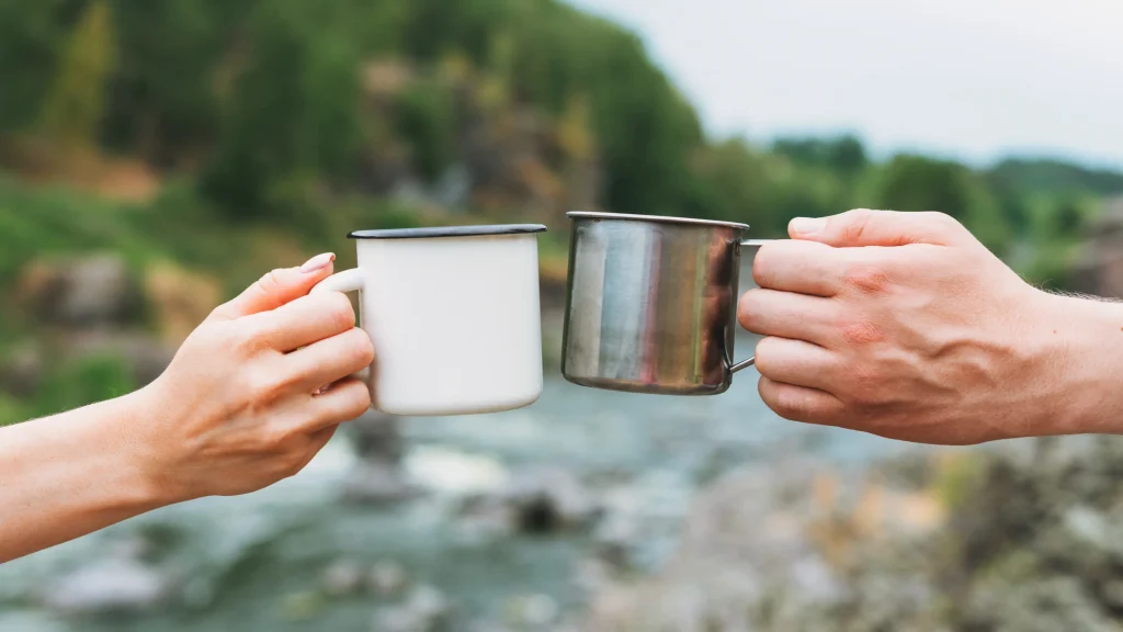 nomad-blog-duo-bag-5 hands of two people clinking tin cups above a river